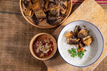 Fried rice with fried catfish in a white porcelain bowl Chili fish sauce in a wooden cup On a wooden chopping board garnished with coriander and red pepper. covered with reed mats