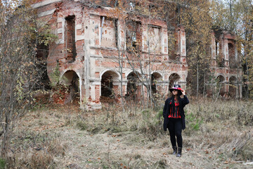A woman in the image of Baron Saturday poses against the backdrop of an old ruined brick building....