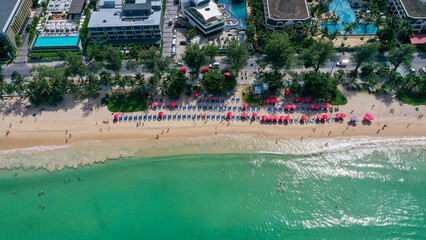 View from above of the clear sea water with tourists enjoying the beach on sun bed with red umbrella in Patong beach