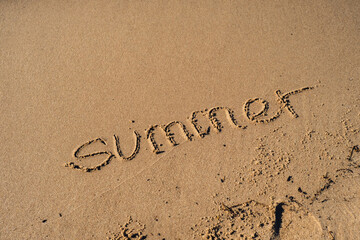 Text SUMMER handwritten in sand surface. Blue ocean wave washing away message at the beach. Summer holidays beach writing vacation concept