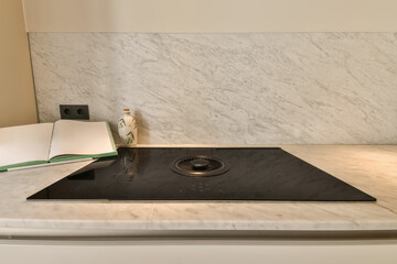 a white marble counter top with a black burner and an open book on the side, next to it