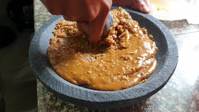 Palm sugar and ingredients being mashed into sweet sticky syrup with mortar and pestle, close up of food preparation action