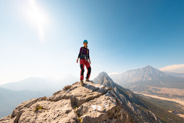 Fototapeta premium young girl climber in a helmet and with a backpack walks along a mountain range against the backdrop of mountains and climbing and hiking.
