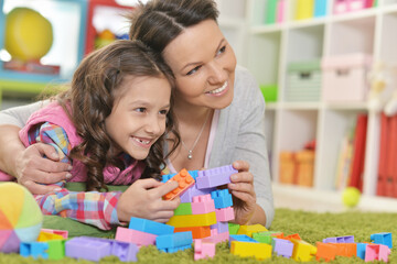 Fototapeta premium Curly little girl and her mother playing with colorful plastic blocks