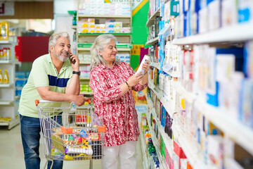 Senior man talking on smartphone and woman shopping at grocery shop.