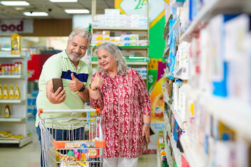 Senior couple talking on video call,using smartphone while shopping at grocery shop.