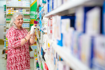 senior indian woman looking some product and purchasing at grocery shop.