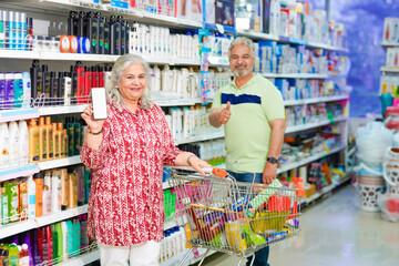 Senior woman showing smartphone with her husband at grocery shop