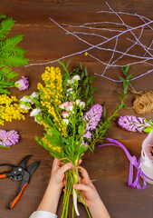 Florist at work: woman making fashion modern bouquet of different flowers on wooden background.