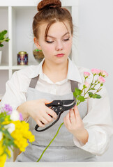 Cute girl florist collects a bouquet in a flower shop. A beautiful florist creates a composition of flowers. Girl cuts flowers and removes stale leaves.
