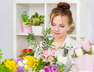 A young girl florist makes a bouquet in a flower shop. Celebration decoration concept