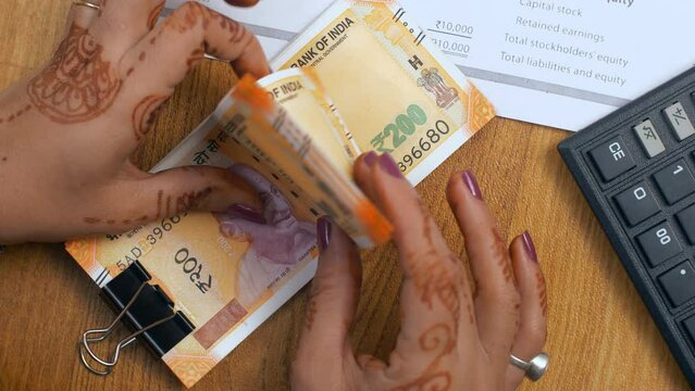 A female accountant is counting a bundle of two hundred rupees - Indian banknotes  Indian currency  denominations. Bank cashier counting Indian currency notes - office desk  financial documents  bu...