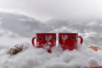 two red mugs with heart shaped on the snow and mountain background- valentine concept