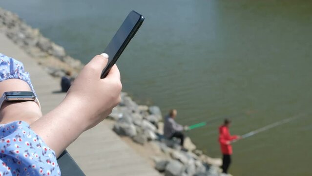 The girl sits on a bench, and scrolls through the pictures in the phone, ea promenade of the sea.