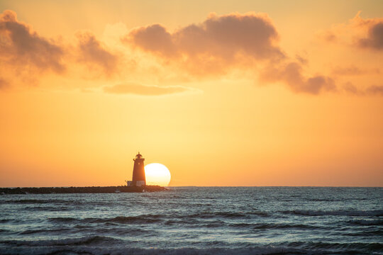 Partial sun rising behind lighthouse in Ireland with yellow sky