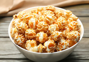 Bowl with tasty caramel popcorn on wooden table MADE OF AI