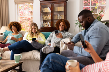 Happy diverse group of friends using smartphones with cups of coffee at home