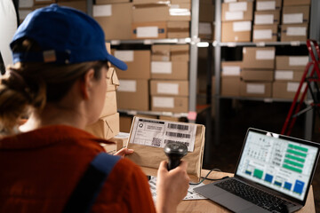 Woman worker working with warehouse management system with barcode reader and laptop computer. Girl working in factory warehouse scanning labels on the boxes with barcode scanner. - obrazy, fototapety, plakaty