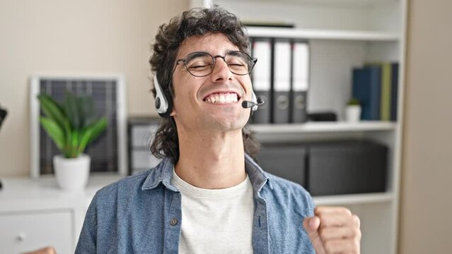 Young hispanic man business worker using computer and headphones with winner gesture at office