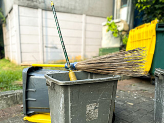 Trash bin, broomstick, and rubbish scoop located behind the house
