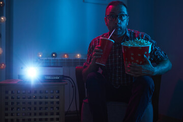 Man enjoying popcorn and juice while watching movie at home projector.