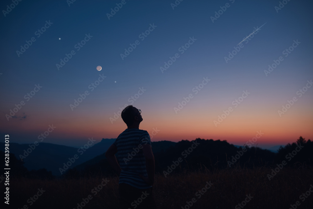 Wall mural man looking at the starry skies, crescent moon and shooting star in blue hour twilight time.