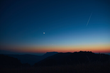 Silhouette of a countryside with Milky Way stars, shooting star, planets and crescent Moon.