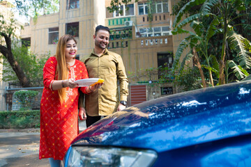 Young indian couple standing with new car. woman holding puja thali in hand.