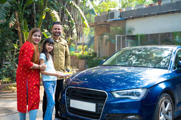 Indian family standing with new car. girl holding puja thali in hand.