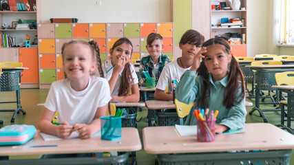 Elementary School and People Concept. Diverse excited group of emotional happy junior school kids sitting at desks in classroom