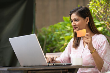 Happy Indian woman using laptop and showing bank card. Digital payment concept.