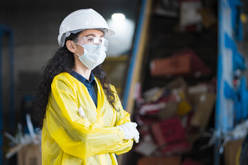 Black-haired female inspector standing against conveyor belt at waste recycling plant. Woman...