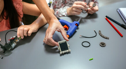Female hand showing solar panel while students assembling machine pieces
