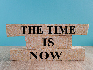 The time is now - words on brick blocks with letters, the time is now concept, blue background, wooden table.