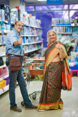 Senior indian couple showing thumps up at grocery shop.