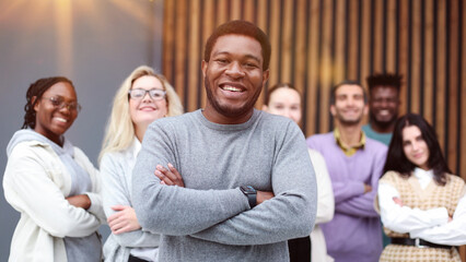 Portrait of a young businessman in the office standing in front of colleagues with their hands folded