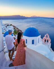 Couple watching the sunset on vacation in Santorini Greece, men and women visit the Greek village of Oia Santorini. - obrazy, fototapety, plakaty