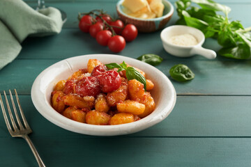 Potato gnocchi. Traditional homemade potato gnocchi with tomato sauce, basil and parmesan cheese on turquoise rustic kitchen table background. Traditional Italian food. Top view.