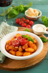 Potato gnocchi. Traditional homemade potato gnocchi with tomato sauce, basil and parmesan cheese on turquoise rustic kitchen table background. Traditional Italian food. Top view.