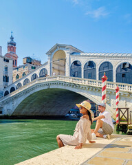 a couple of men and women on a city trip in Venice Italy sitting at the waterfront of the Rialto...
