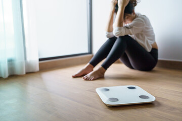 Fototapeta premium Sad woman with fat upset bored of dieting Weight loss fail&nbsp; Fat diet and scale sad asian woman on weight scale at home weight control