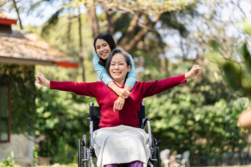 Asian senior woman in wheelchair with happy daughter. Family relationship retired woman sitting on wheelchair in the park age care at retirement home.