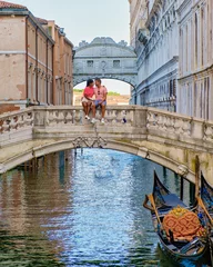 Photo sur Plexiglas Pont des Soupirs a couple of men and women on a city trip in Venice Ital sitting at the waterfront of the bridge of sighs in Venice, Italy. Architecture and landmark of Venice. cityscape of Venice Italy during summer