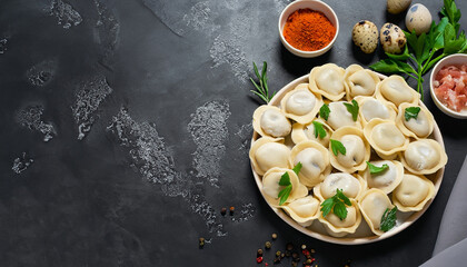 Traditional russian pelmeni, ravioli, dumplings with meat on black concrete background. Parsley, quail eggs, pepper, rosemary, bay leaf and spices. Top view. Copyspace - obrazy, fototapety, plakaty