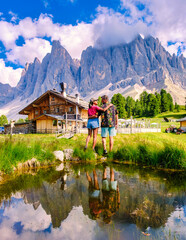 Couple men and women at Geisler Alm, Dolomites Italy, hiking in the mountains of Val Di Funes in Italian Dolomites Adolf Munkel Trail, Nature Park Geisler-Puez with Geisler Alm Puez Odle Nature Park - obrazy, fototapety, plakaty