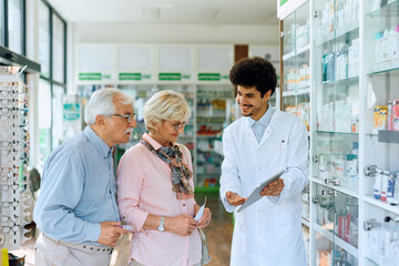 Fototapeta na wymiar Happy pharmacist and senior couple using digital tablet in pharmacy.