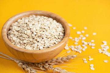 Rolled oats, oat flakes in wooden bowl on yellow background. Summer agriculture food harvest concept