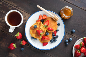 Pancakes with berries and honey on wooden table, top view. Sweet breakfast or brunch meal