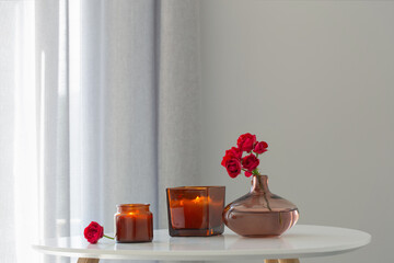 red roses in  vase with burning candles in white interior