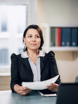 immagine primo piano di donna manager , mezza età, seduta alla scrivania con documenti nelle mani, professionalità e competenza, ambiente di lavoro sfuocato